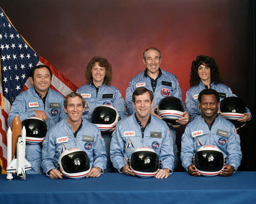 Figure 2. STS-51-L crew: (front row) Michael J. Smith, Dick Scobee, Ronald McNair; (back row) Ellison Onizuka, Christa McAuliffe, Gregory Jarvis, Judith Resnik. Image by NASA - NASA Human Space Flight Gallery, Public Domain.